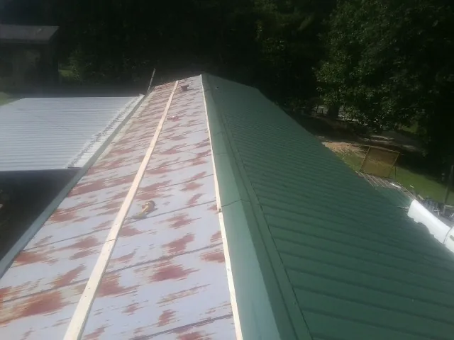 Old rusted panels beside newly installed green metal roofing — Wind Damage Roof Repair by Roofing Brothers in Drewsville