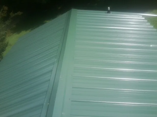 New green metal panels meeting at the ridge of a roof — Flat Roof Repair work by our crew in Drewsville