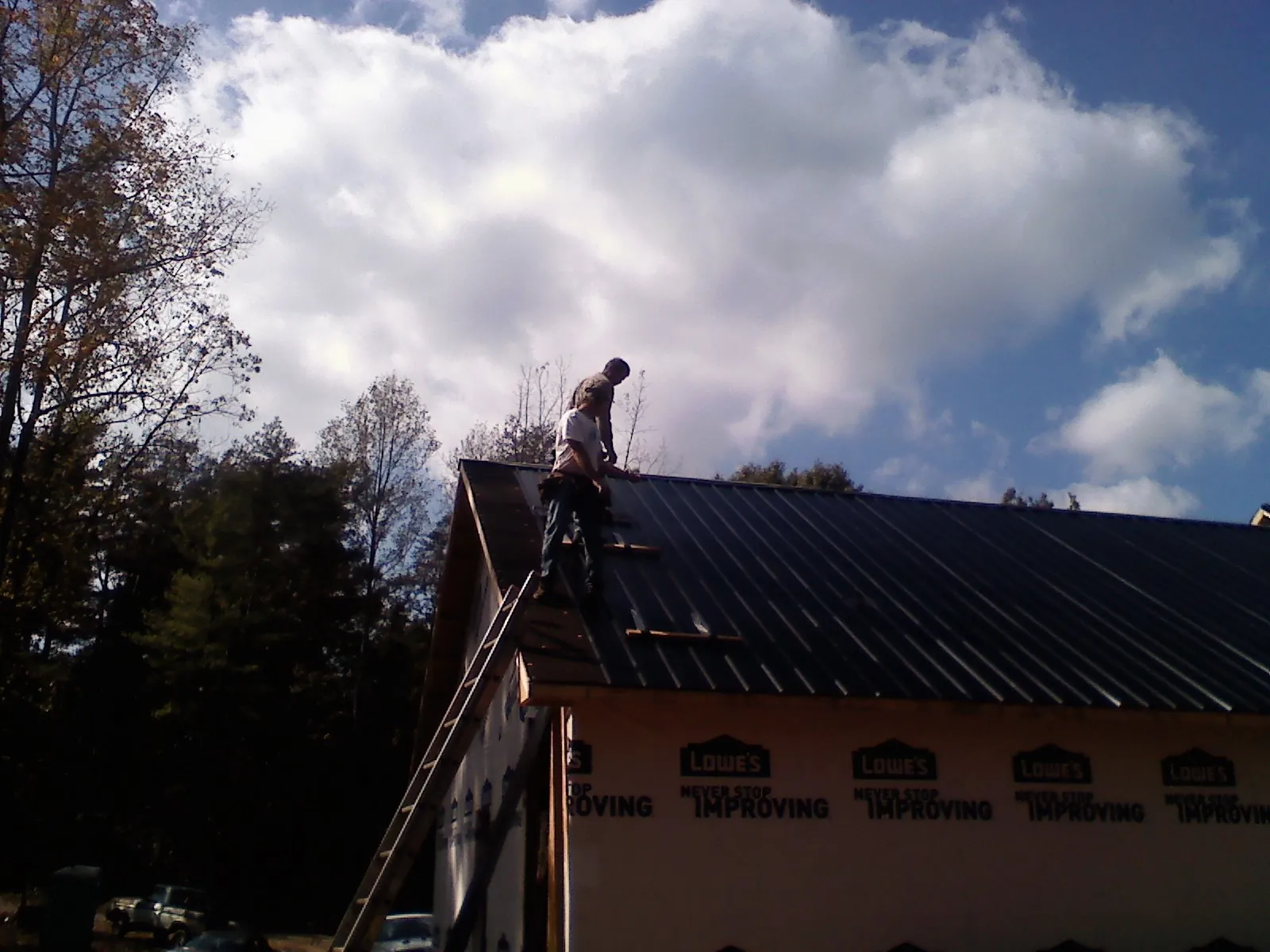 Roofer fastening dark metal panels high against a cloudy sky, from a Roof Inspection job in Drewsville