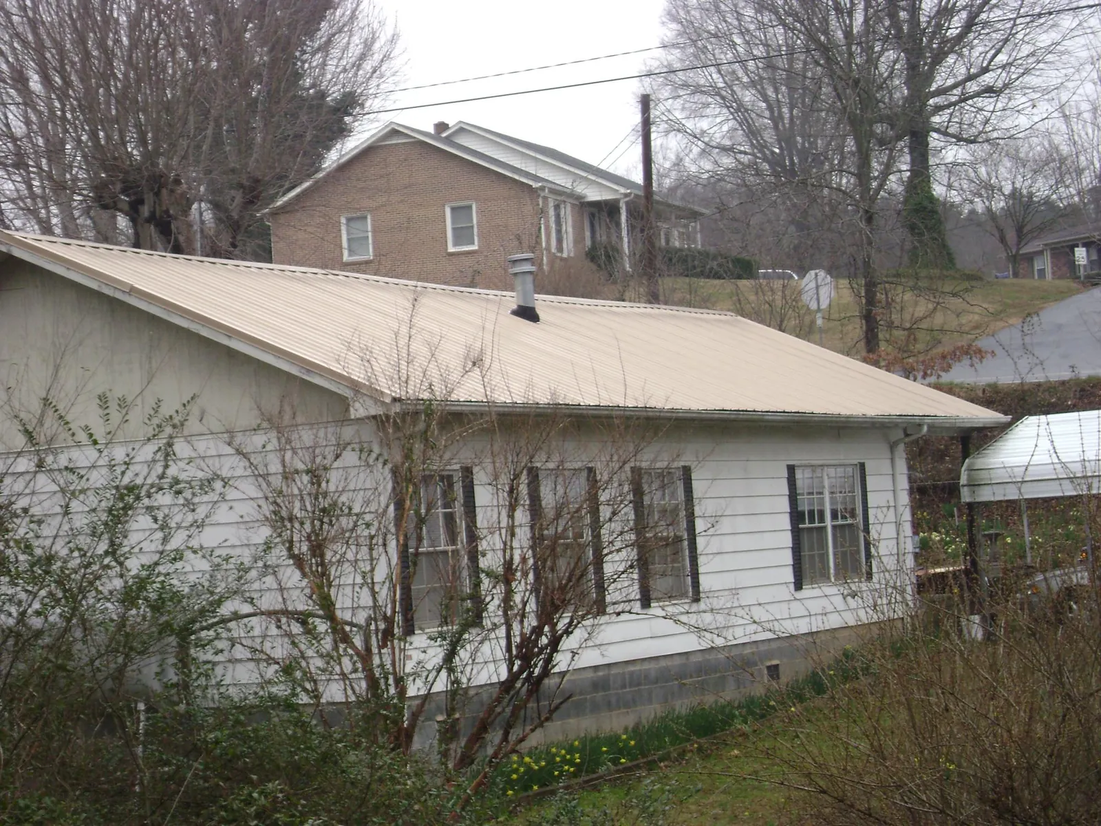 Tan metal roof on a white sided house set into a hillside — Commercial Roofing by Roofing Brothers in Drewsville